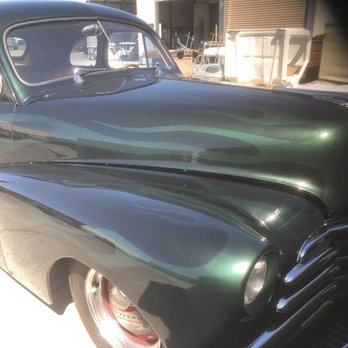 A dark green classic car with ghost flame paint on the hood and fenders