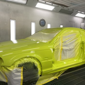A bright green car masked and ready for paint inside a paint booth